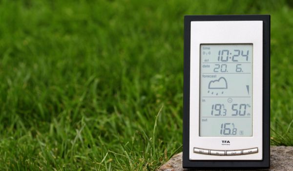 Nahaufnahme einer digitalen Wetterstation auf einem Stein. Im Hintergrund grüne Wiese.
